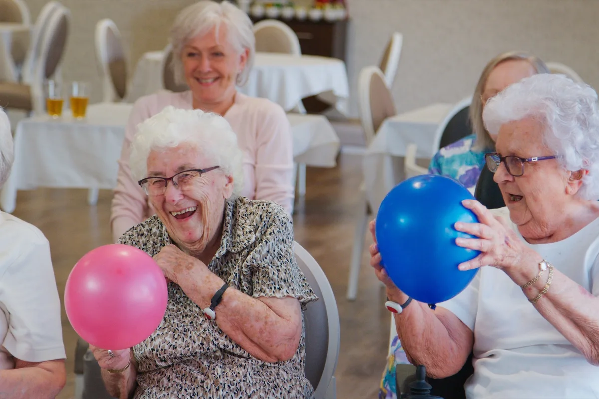 Un grupo de adultos mayores ríe mientras juega con globos durante una actividad en grupo