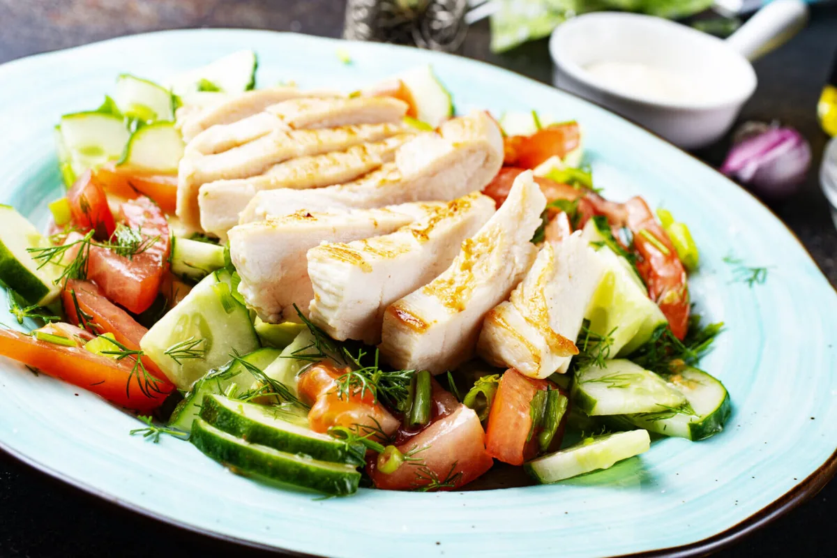 Plato servido con pollo horneado y verduras frescas sobre una mesa