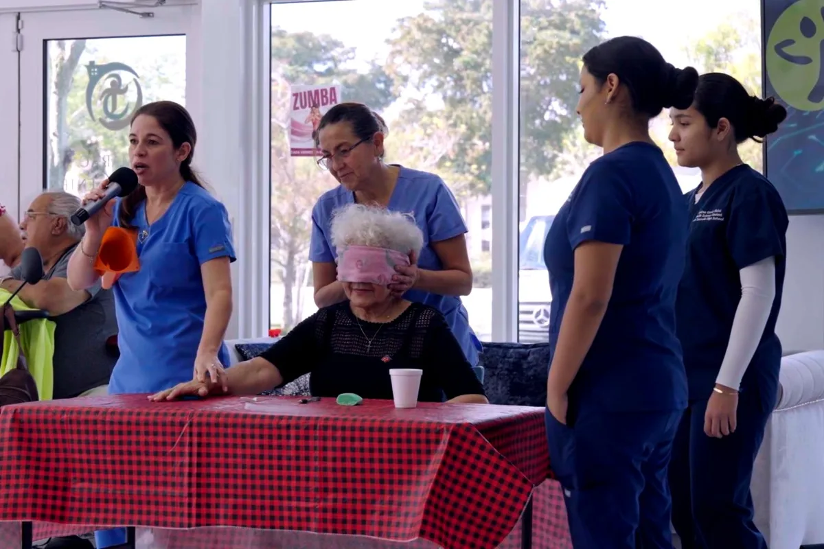 Staff in blue scrubs lead a table activity with members at the adult day center