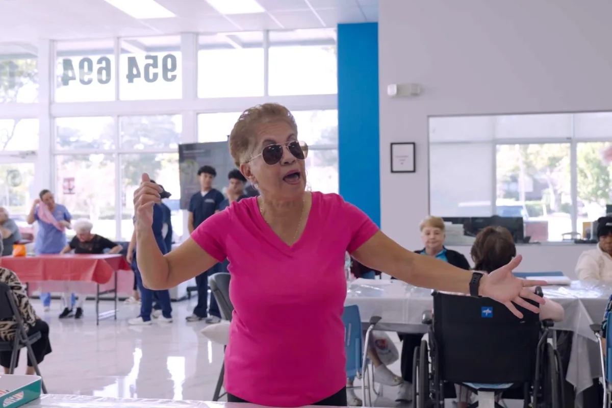 Una señora con blusa rosada extiende los brazos durante una actividad en el salón del centro
