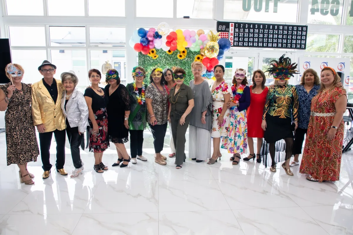 A large group of members in colorful outfits poses together inside the center during a celebration